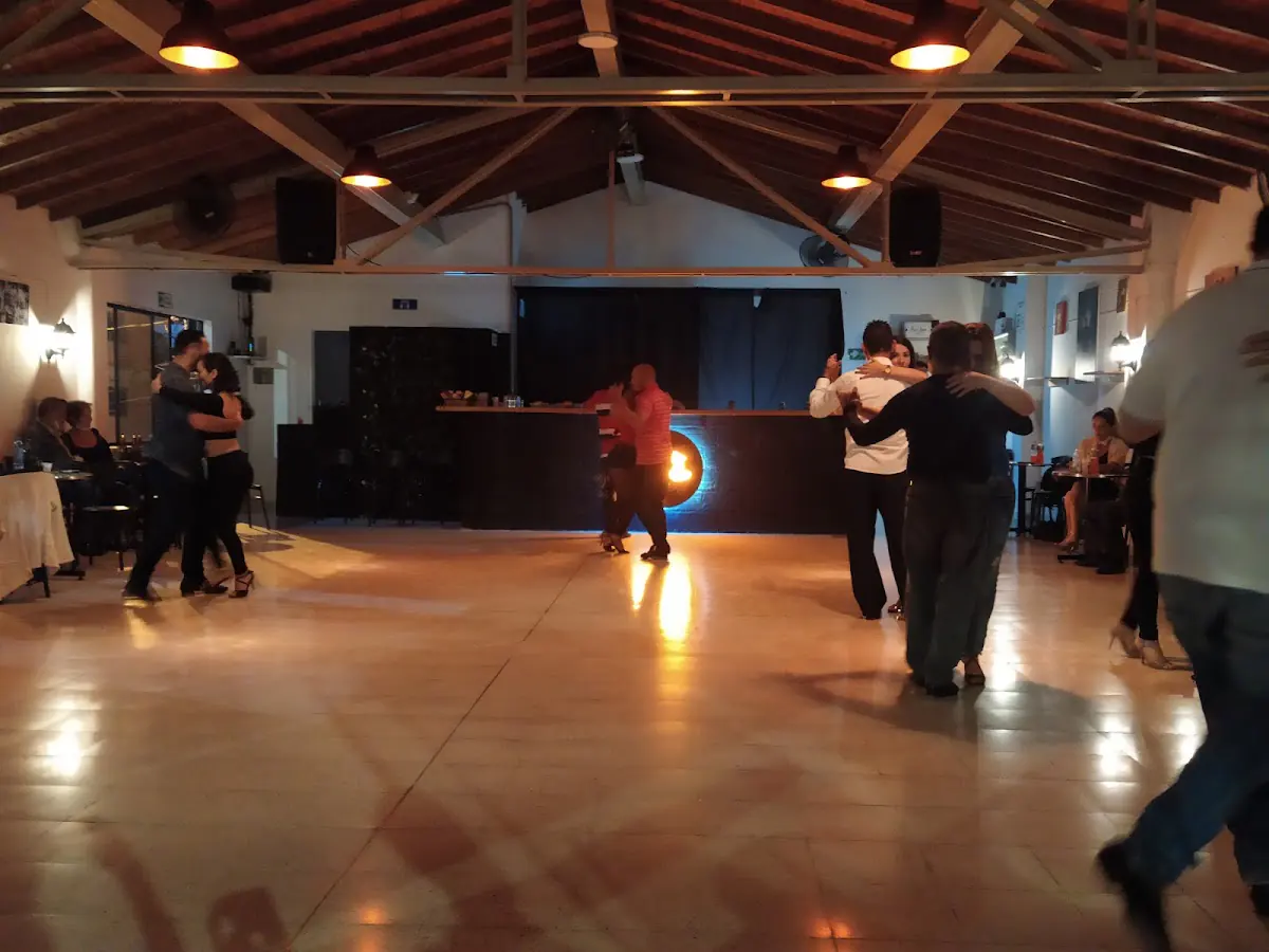Parejas bailando tango en la pista de Nueva Guardia, con el logo iluminado al fondo